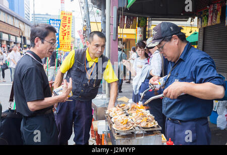 TOKYO, JAPAN - 18 JULY 2016 - Tourists watch street vendor cooking seafood snack at Tsukiji Fish Market in Tokyo, Japan on July 18 2016.