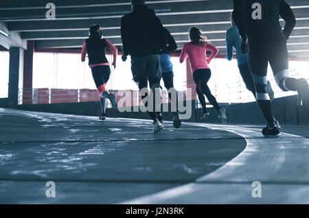 Back view of athletes in sportswear running on race track in gym. Stock Photo