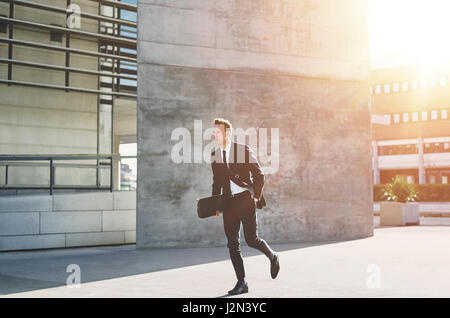 A modern businessman dressed in suit walking with the skateboard in the street. Stock Photo