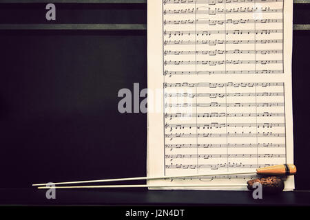 music sheets and conductor's batons on black metal stand in warm retro color tone, with room for copy space Stock Photo