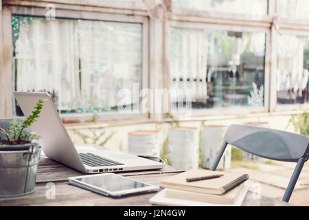 Outdoor work table with laptop computer, tablet, phone, and other stationery in selective focus on computer screen, vintage tone Stock Photo