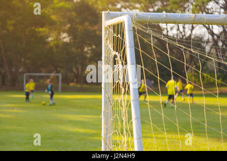 corner of a soccer or football goal post with warm morning light and blurred players and field in background Stock Photo