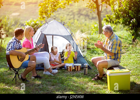 parent and children enjoying with guitar in a tent Stock Photo