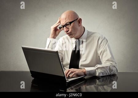 Stressed bald businessman working on laptop Stock Photo