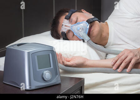 Asian man with sleep apnea using CPAP machine, wearing headgear mask connecting to air tube Stock Photo