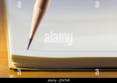 Close up of pencil's tip on blank white notebook paper with long skinny shadow, on wooden table, selective focus on the tip of pencil Stock Photo