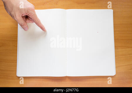 Four hands with finger pointing at blank white paper notebook on wood table Stock Photo