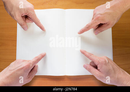 Four hands with finger pointing at blank white paper notebook on wood table Stock Photo