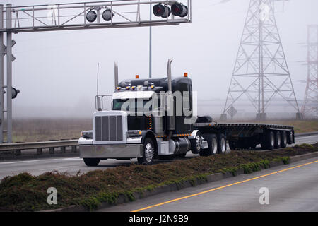 Stylish classic semi truck with chrome body trim and a flat bed trailer on the road with the traffic separation with traffic lights and restrictive Stock Photo