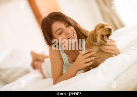 Pretty young female owner of the puppy gently caressing him in bed Stock Photo