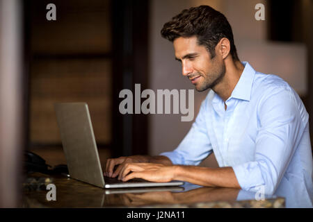Portrait of a nice smiling man working at home on some project, he is sitting at a table looking at his laptop in front of him Stock Photo