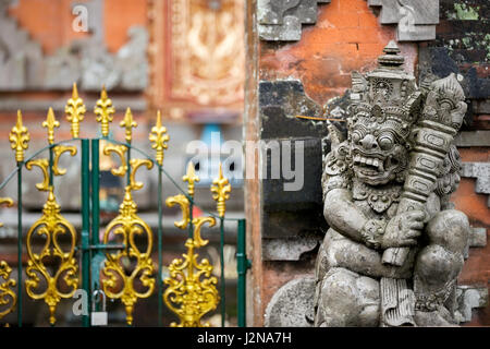 Traditional guard demon statue carved in dark stone in front of the gate of Hindu temple in tropical Bali Stock Photo