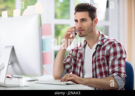 Male office worker front computer talking on phone Stock Photo