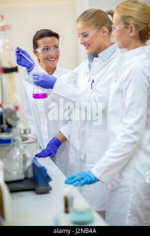 Young chemical assistants taking sample and analyzing fluid from flask in laboratory Stock Photo