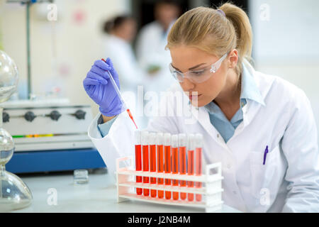 Young female chemist taking sample with pipette in laboratory Stock Photo