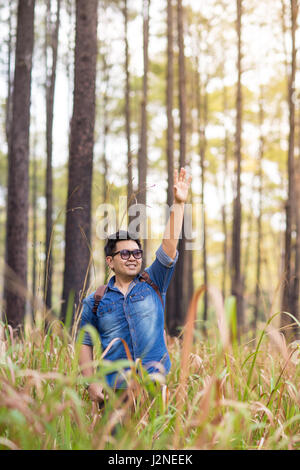 An Asian man use hand gesture waving to call someone or saying hello in the pine forest. Stock Photo