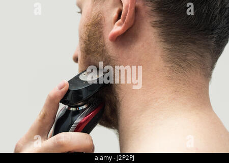 young man shaving his beard off with an electric shaver Stock Photo