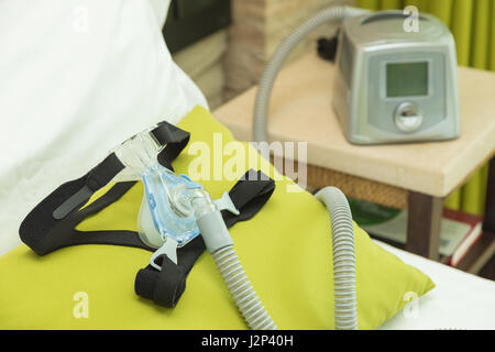 CPAP headgear mask with air tube connecting to CPAP machine in bedroom Stock Photo