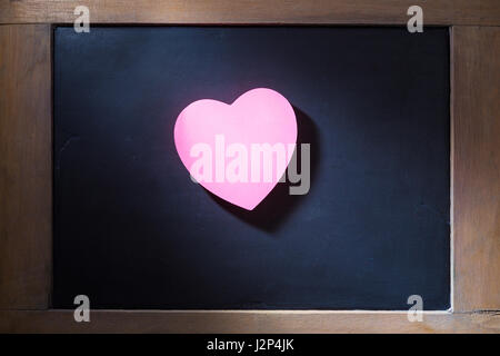 Empty pink hearted shape post-it note on blackboard with concentrated light beam for dramatic feel, vintage retro look Stock Photo