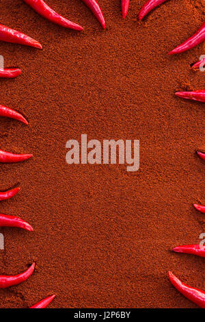 chili red hot pepper, concept of popular spice - sharp tips of red chili peppers laid out in a frame on background of dry mix of brown curry powder, flat lay, top view, free space for text. Stock Photo