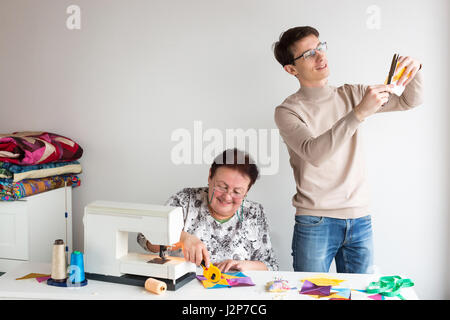 patchwork - the work of the two tailors in the studio - woman cut with scissors colored fabric behind table with fabrics and tools, a handsome man stands by and cuts with scissors patchwork fabric. Stock Photo