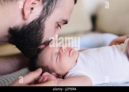 A young father kisses his sleeping newborn son. Father and newborn baby closeup. Father and newborn lying on the bed. Stock Photo