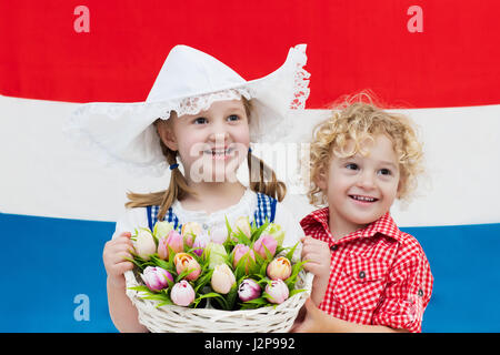 Little Dutch girl and boy wearing traditional national costume, dress and hat holding basket of tulips at flag of the Netherlands. Children with souve Stock Photo