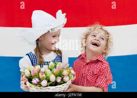 Little Dutch girl and boy wearing traditional national costume, dress and hat holding basket of tulips at flag of the Netherlands. Children with souve Stock Photo