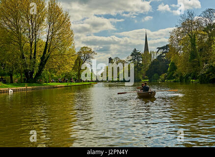 Stratford upon Avon and aAcouple enjoying a trip in a rowing boat on the River Avon, with Holy Trinity church spire in the background. Stock Photo