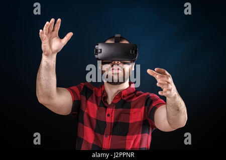 Young man using VR glasses headset trying to touch objects in virtual reality. Stock Photo
