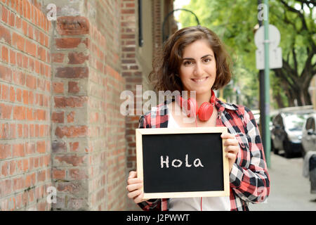 Young beautiful woman holding chalkboard with text 'Hola'. Outdoors. Stock Photo