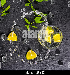 mojito cocktail with splash, ice, green mint, limes and drops on black slate background, close up Stock Photo