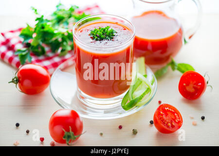 tomato juice in glass, jug with greenery, basil, cutted tomato fruit and dry pepper on light table, concept healthy eating, close up Stock Photo