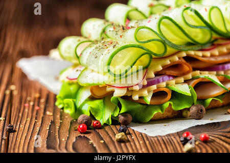 healthy sandwich made of ham, cheese, bacon, radish, lettuce, cucumbers and onions decorated dry pepper on dark wooden background Stock Photo