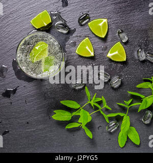 mojito cocktail with splash, ice, green mint, cuted limes and drops on black slate background, close up Stock Photo