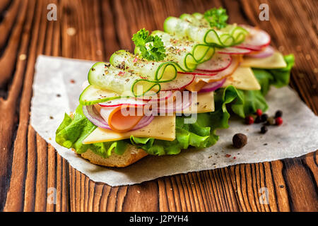 sandwich with ham, cheese, bacon, radish, lettuce, cucumbers and onions decorated dry pepper, parsley on dark wooden background, close up Stock Photo