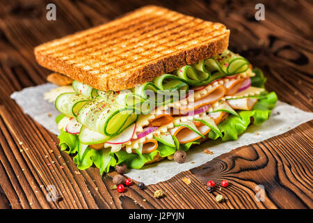 sandwich with grilled toast, ham, cheese, radish, lettuce and cucumbers decorated dry pepper on dark wooden background Stock Photo