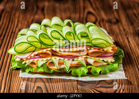 rich sandwich with ham, cheese, bacon, radish, lettuce, cucumbers and onions on dark wooden background, concept of healthy eating Stock Photo