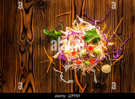 top view of finely chopped white, red cabbage, carrot decorated red pepper, cucumber, parsley over wooden background, concept healthy eating Stock Photo