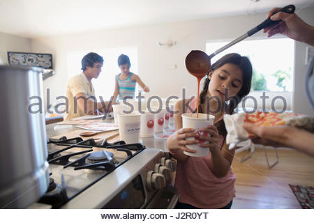 Mother and daughter cooking soup, pouring into container in kitchen
