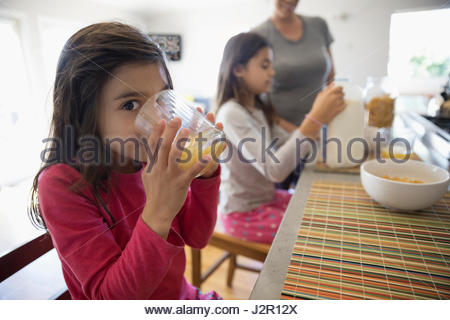 Portrait smiling girl drinking orange juice at breakfast bar in kitchen