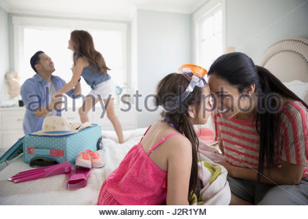Playful mother and daughter rubbing noses on bed, packing for vacation