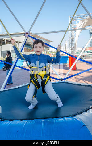 A young boy bouncing on a trampoline with bungie ropes attached to allow him to jump higher. Stock Photo