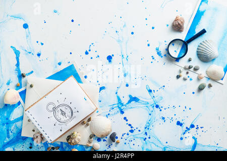 Marine travel flatlay with seashells, sketchbook, magnifying glass and compass drawing on a watercolor background Stock Photo