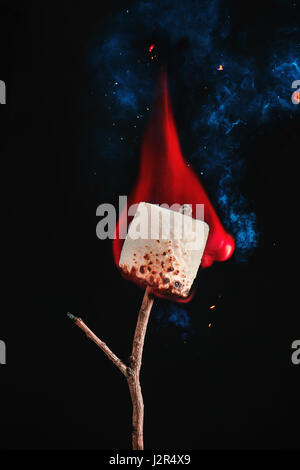 Close-up of a perfectly roasted marshmallow with flame, sparks and smoke on a black studio background Stock Photo