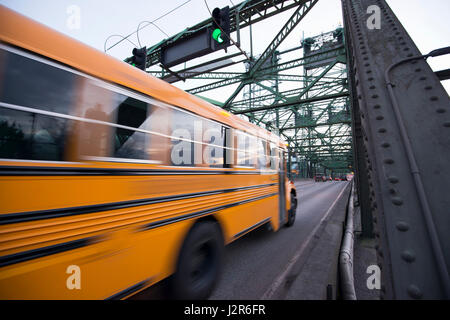 Long blurred in motion yellow school bus moves on the metal truss bridge with a green traffic light Stock Photo