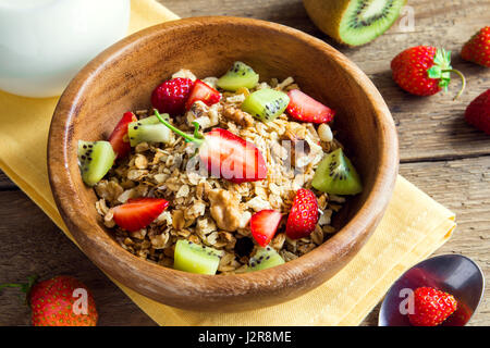 Homemade granola with fruits (strawberry and kiwi) in wooden bowl for healthy breakfast close up Stock Photo