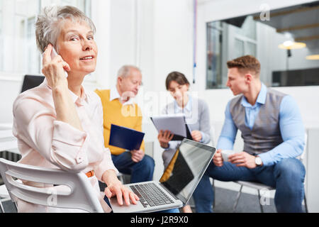 Senior business woman in meeting using phone and listening Stock Photo