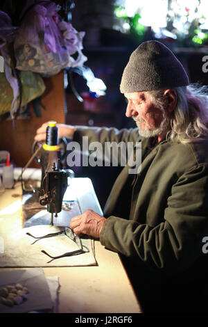 A senior adult man sewing a piece of cloth on a sewing machine. Stock Photo