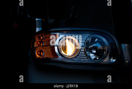 Modern big rig semi-truck turn on head light with details in dark background Stock Photo